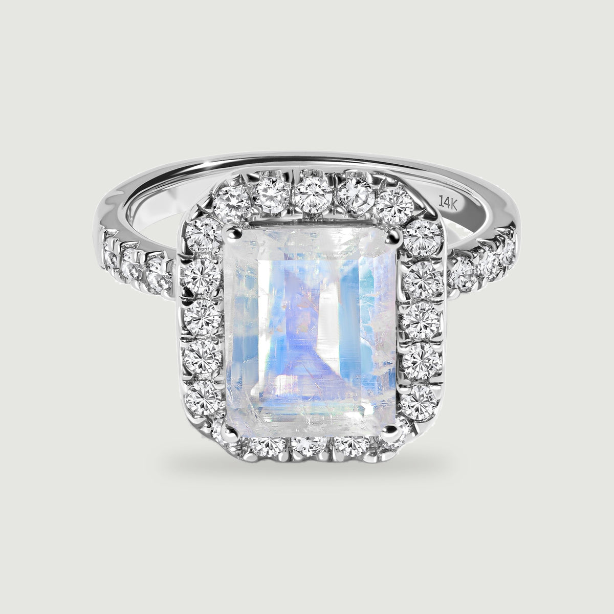 A white gold ring displays a blue-flashing rectangular moonstone within a border of round diamonds.
