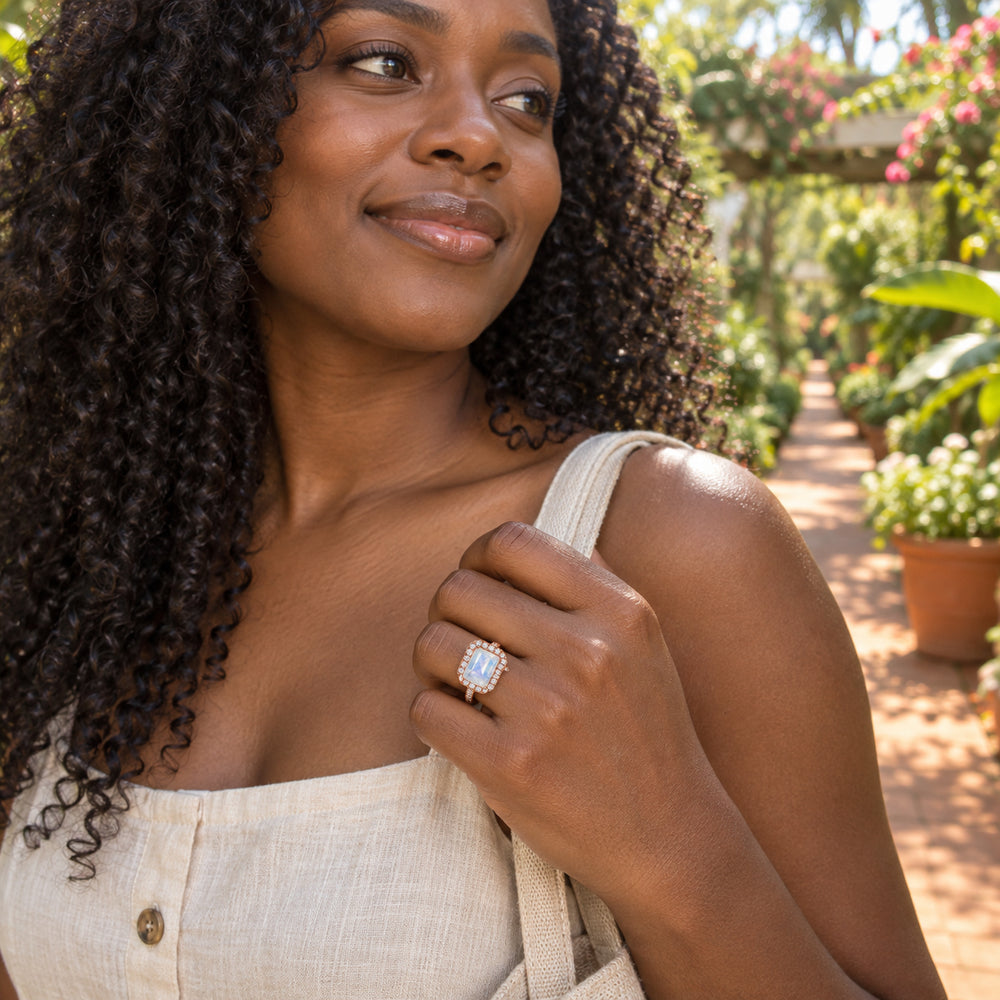 A woman with curly hair wears the rose gold moonstone ring while holding a linen strap in a sunlit garden.