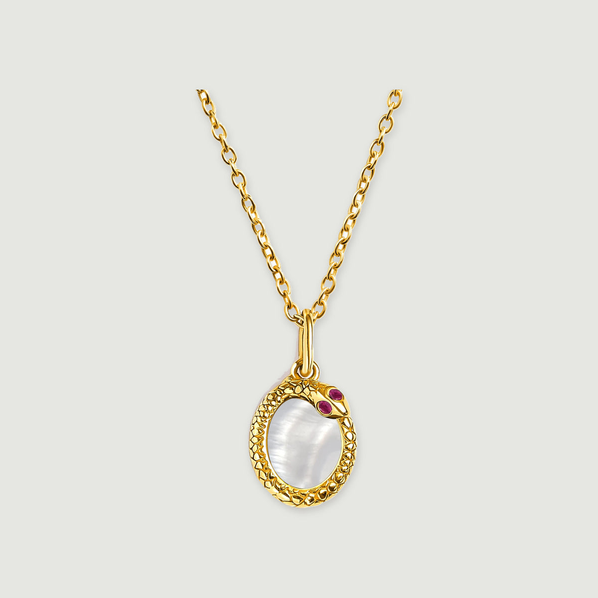 A yellow gold plated necklace shows a pale oval mother of pearl center, a patterned border, and two ruby red accents.
