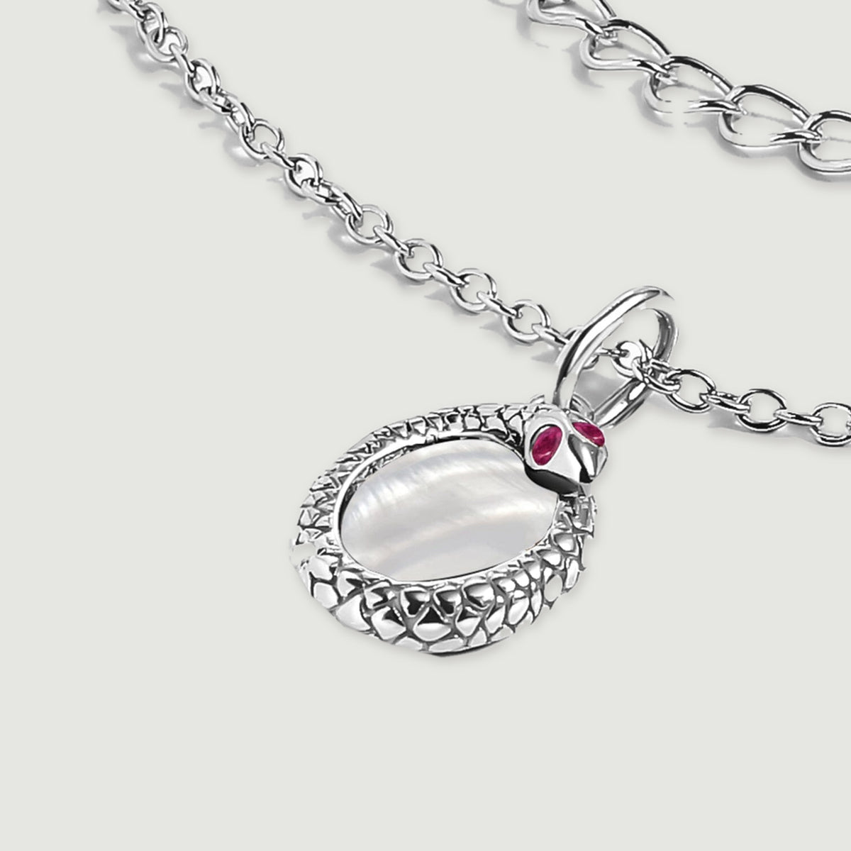 The white rhodium plated pendant lies flat beside curved chain links on a clean light gray surface.