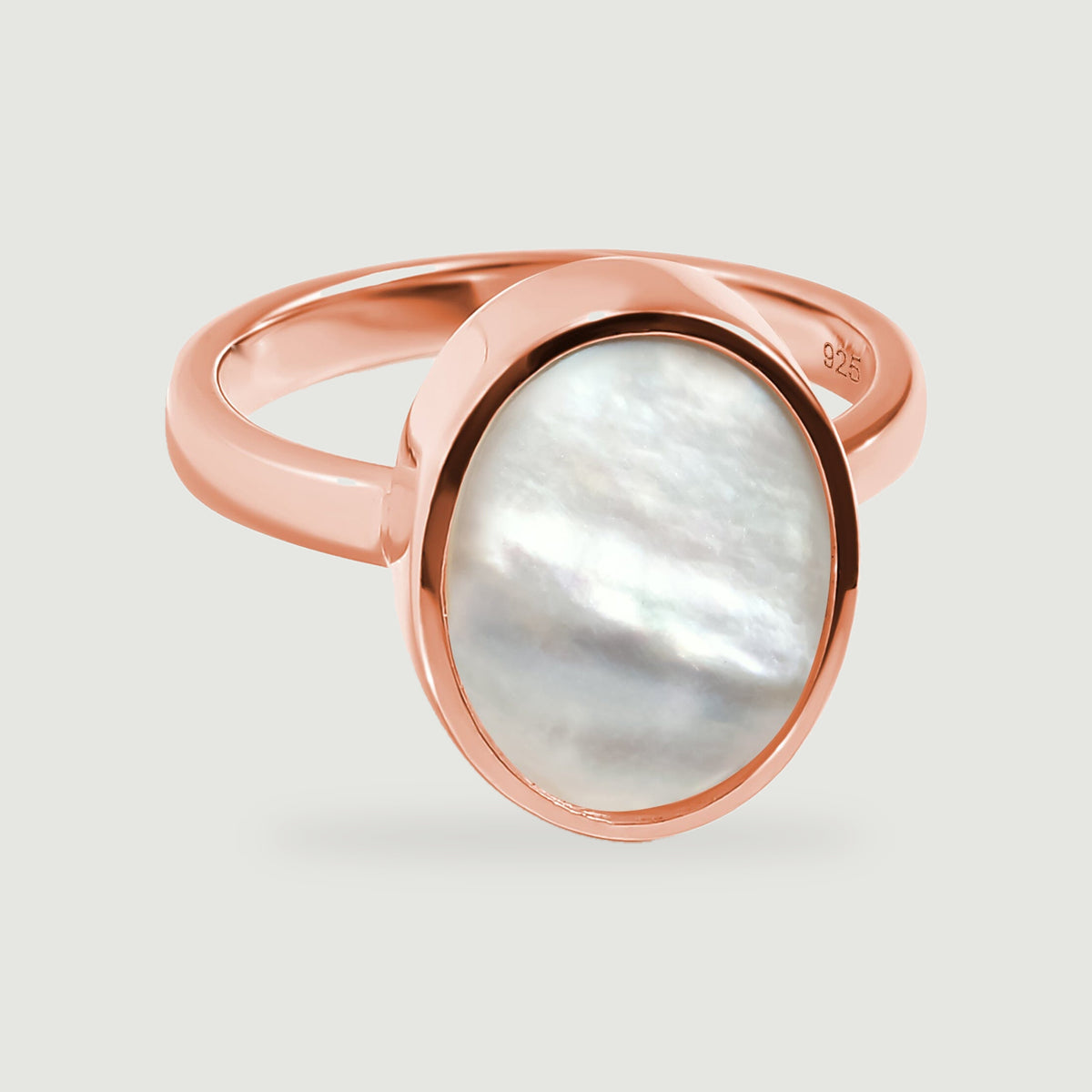 An oval white mother-of-pearl ring with a polished rose gold bezel rests on a light gray surface.