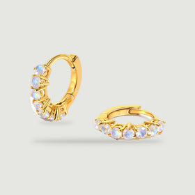 A pair of yellow-gold-tone moonstone hoops rests against a light gray background.