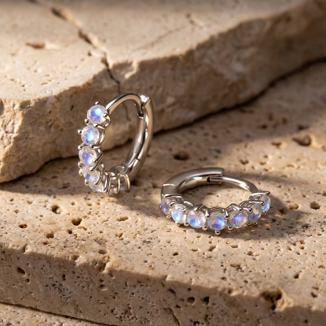 Two silver-tone moonstone hoops are arranged on warm, textured stone slabs.