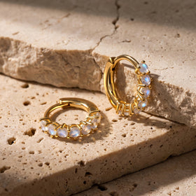 A yellow-gold-tone moonstone hoop stands beside its matching hoop on a beige stone surface.