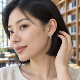 A woman with a black bob wears a small silver-tone moonstone hoop beside wooden library shelves.