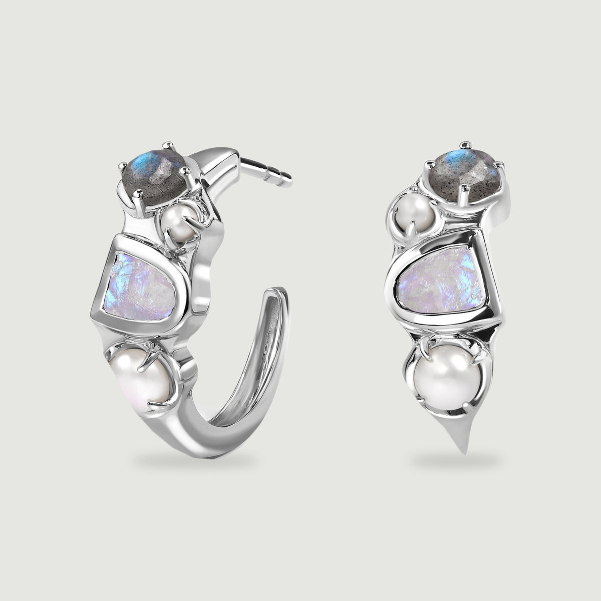A pair of silver-tone open hoop earrings displays blue-flashing stones and two white pearls on each hoop against a light gray background.