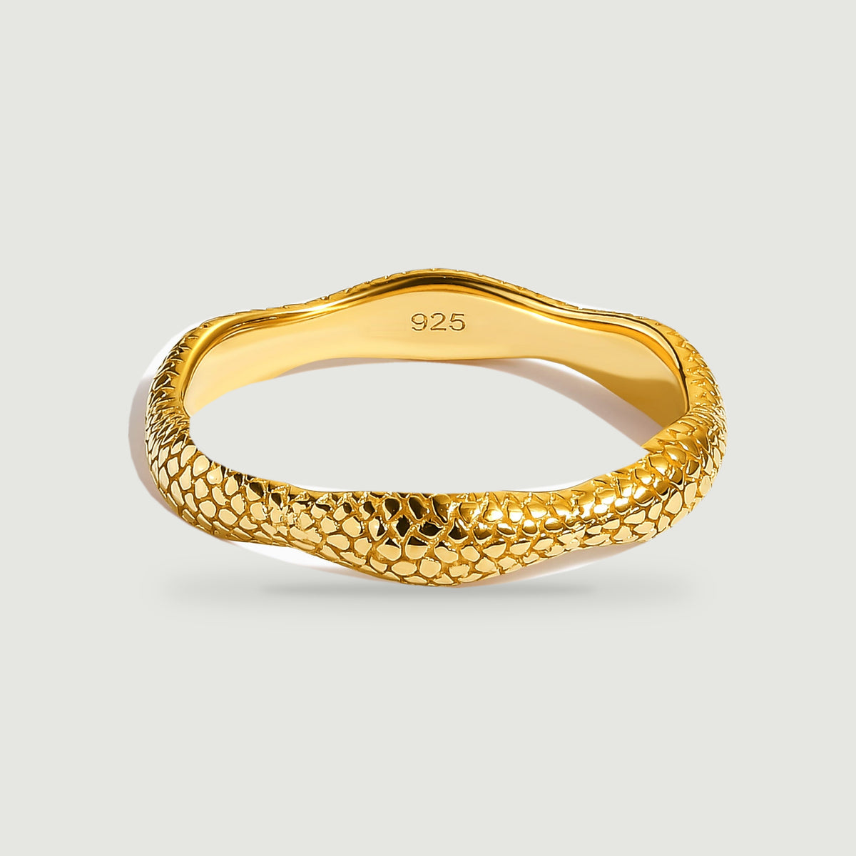 A yellow gold ring shows its textured outer band and smooth inner surface against pale gray.