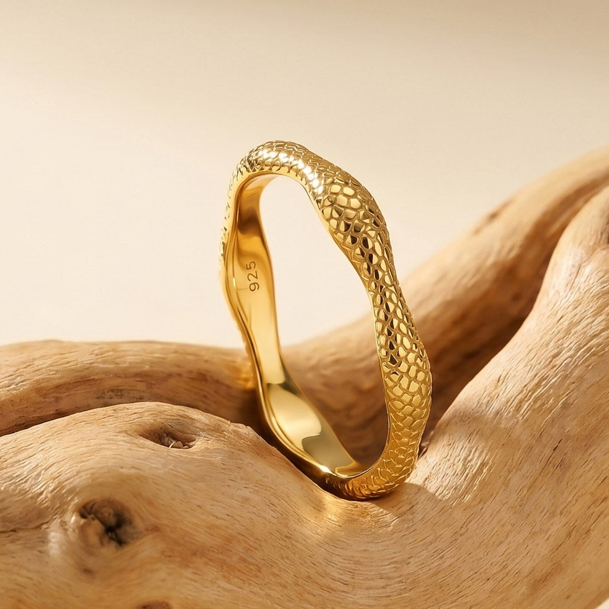 A yellow gold ring stands on driftwood with its wavy edge and polished inner band visible.
