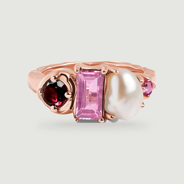 A rose gold ring shows its smooth band behind a red round gemstone, a pink rectangular gemstone, and a softly curved white pearl.