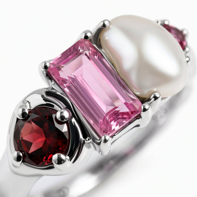 Silver rounded prongs hold a deep red gemstone beside a large pink rectangular stone and a white pearl in a diagonal close-up.