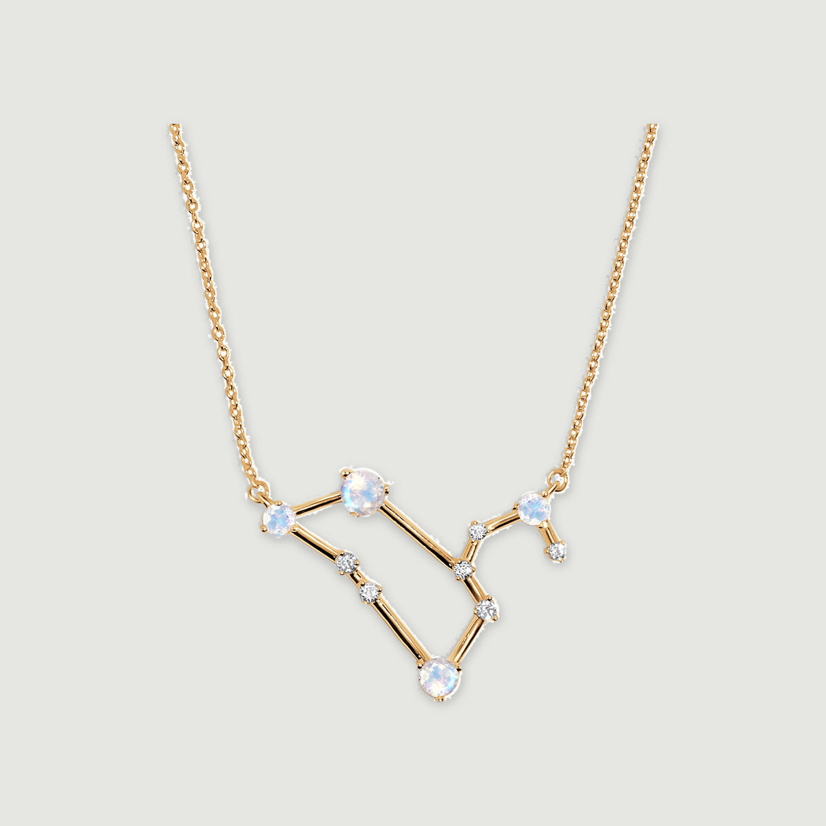 A yellow gold necklace has an angular pendant with four pale blue moonstones and small clear stones on a light gray background.