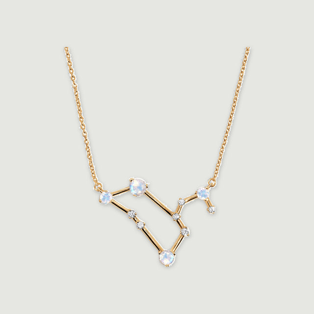 A yellow gold necklace has an angular pendant with four pale blue moonstones and small clear stones on a light gray background.