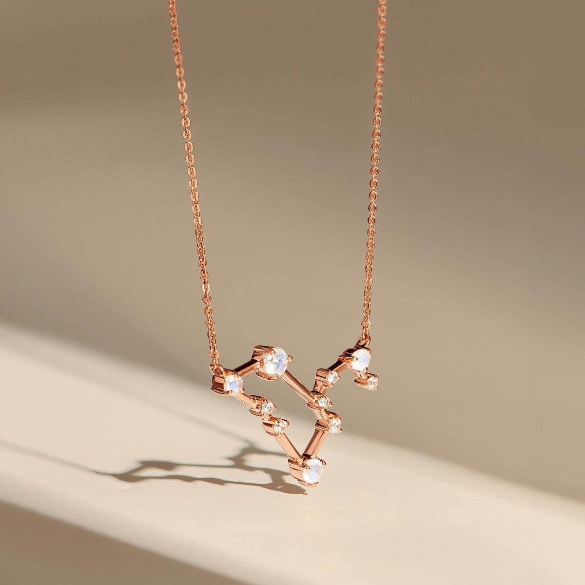 A rose gold pendant hangs above a beige surface, revealing the raised stone settings and fine chain.