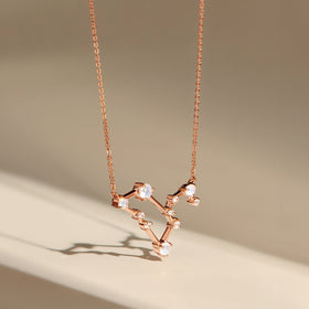 A rose gold pendant hangs above a beige surface, revealing the raised stone settings and fine chain.