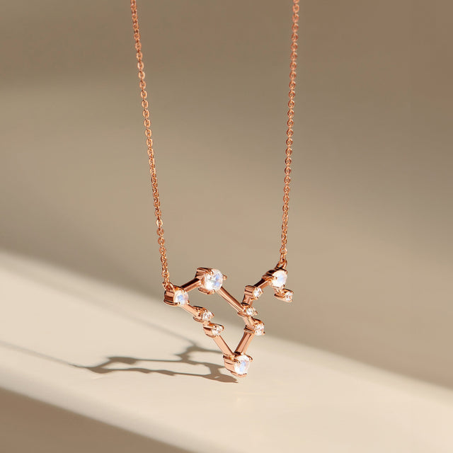 A rose gold pendant hangs above a beige surface, revealing the raised stone settings and fine chain.