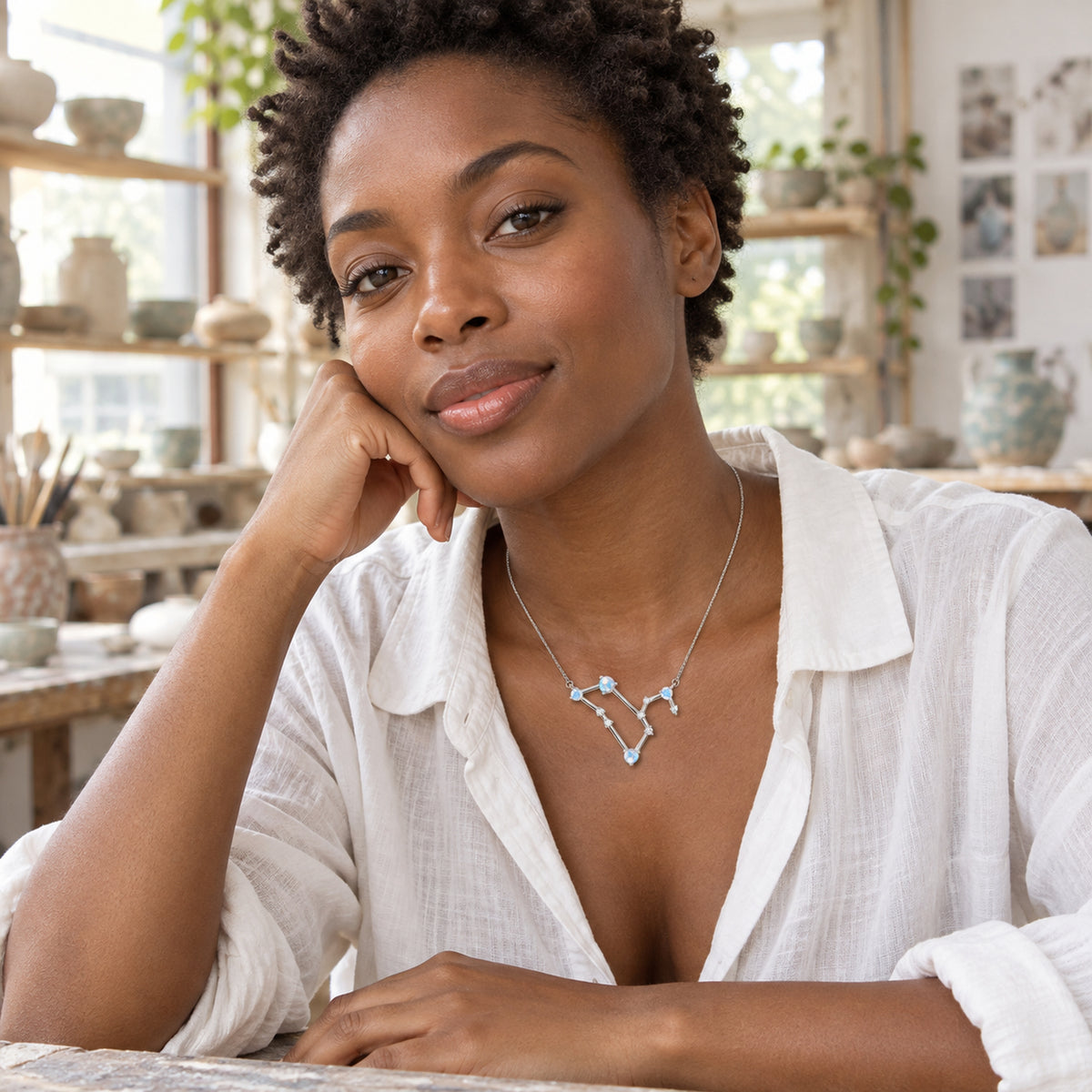 A woman with short coiled hair wears the silver moonstone necklace in a sunlit pottery studio.