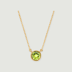A round green peridot in a yellow gold bezel hangs between two fine chain sections on a light gray background.