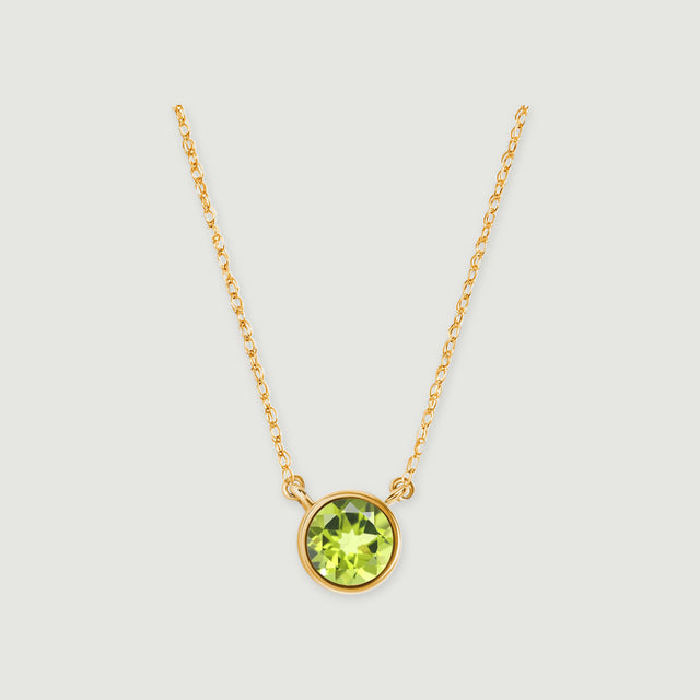 A round green peridot in a yellow gold bezel hangs between two fine chain sections on a light gray background.