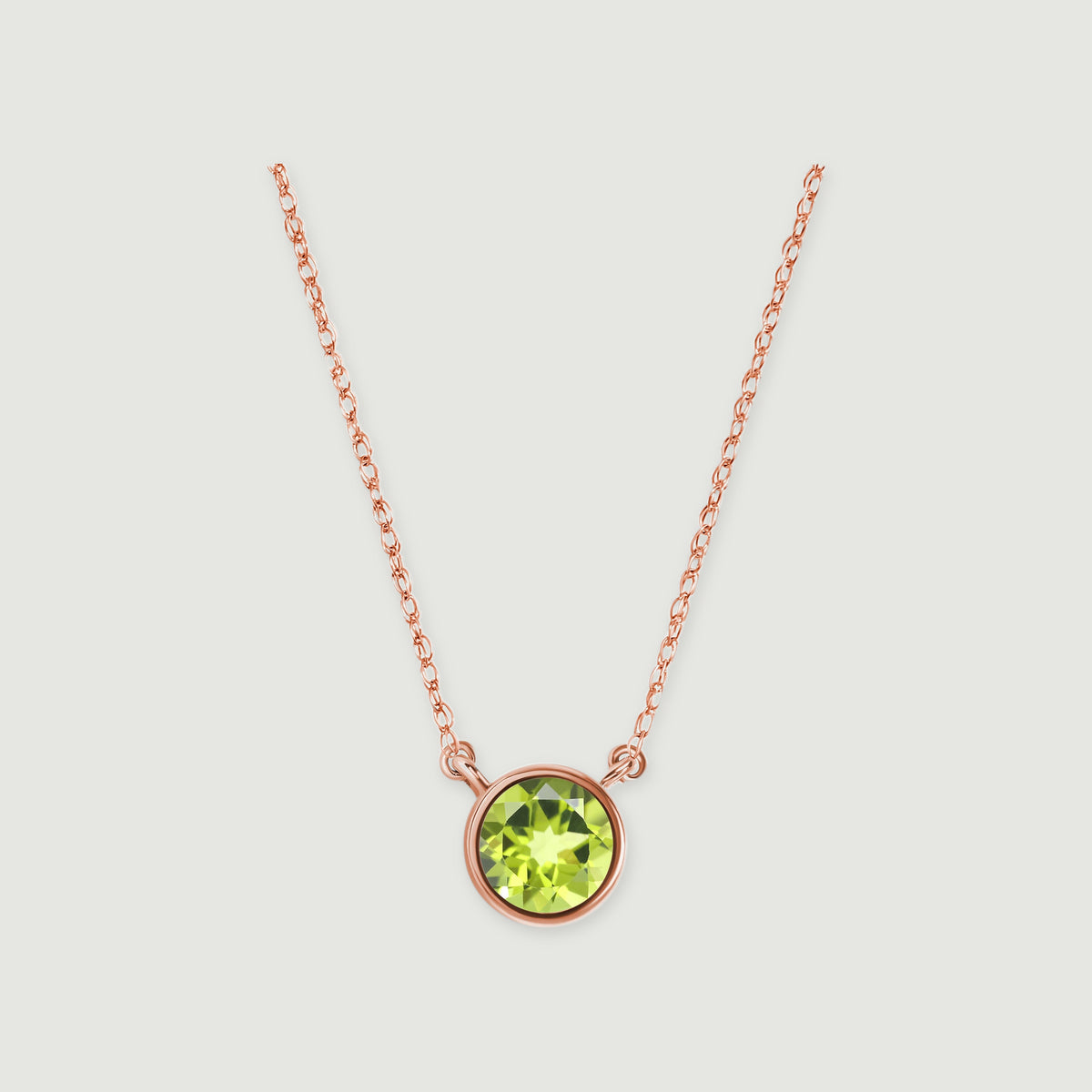 A polished rose gold bezel surrounds a green peridot beneath a delicate open-link chain on light gray.