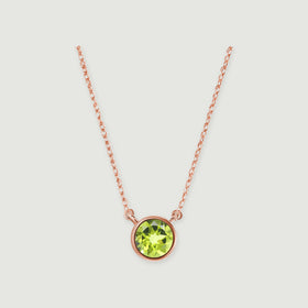 A polished rose gold bezel surrounds a green peridot beneath a delicate open-link chain on light gray.