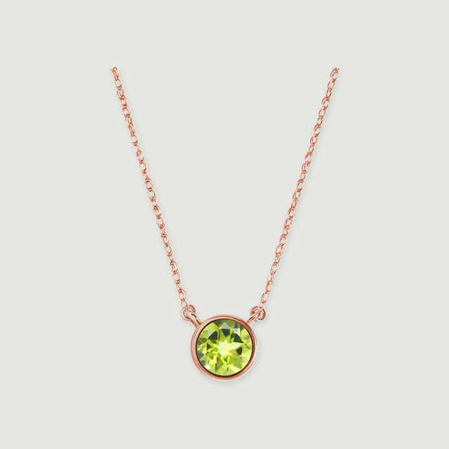 A polished rose gold bezel surrounds a green peridot beneath a delicate open-link chain on light gray.