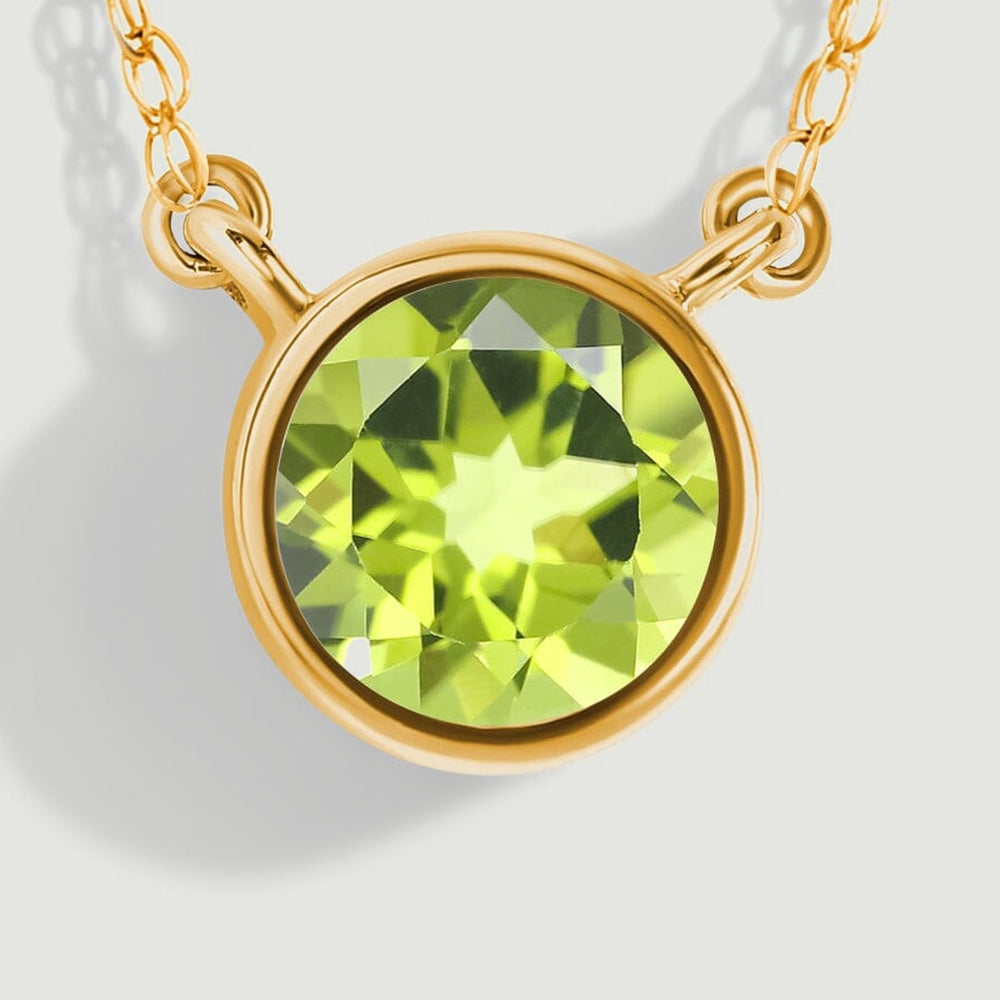 A close view shows the green peridot facets, smooth yellow gold bezel, and oval chain attachment loops.