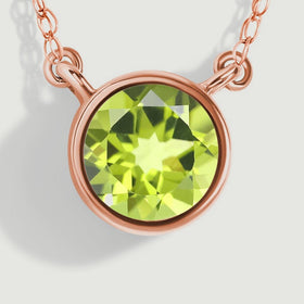 The rose gold rim and two connector loops frame the bright green facets of the round peridot in this close-up.