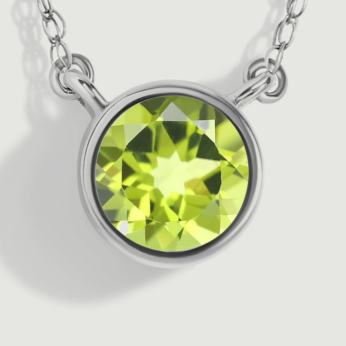 A macro view reveals the white gold bezel edge, open attachment loops, and angular green reflections inside the peridot.
