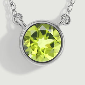 A macro view reveals the white gold bezel edge, open attachment loops, and angular green reflections inside the peridot.