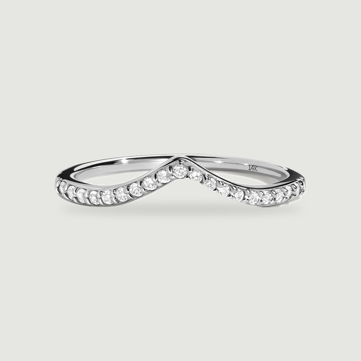 A white gold ring with a pointed diamond-set band rests on a light gray surface.