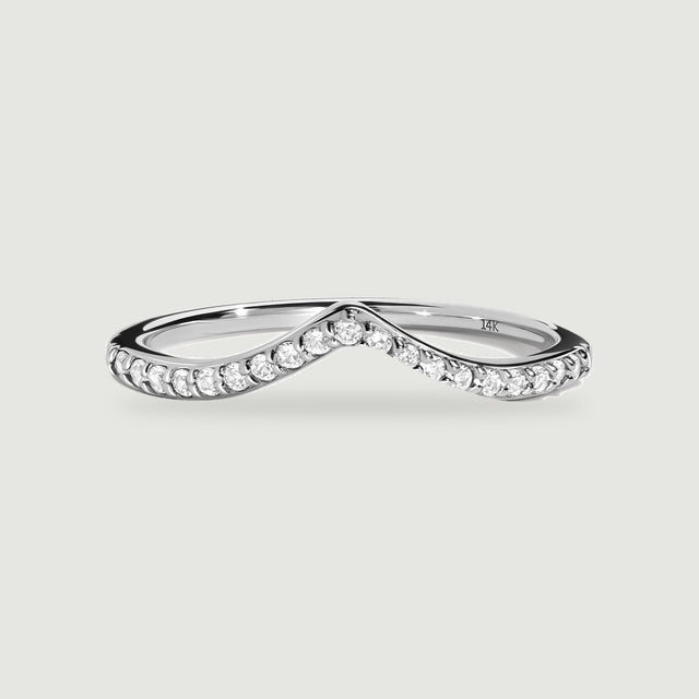 A white gold ring with a pointed diamond-set band rests on a light gray surface.