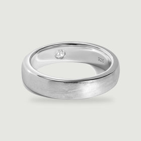 A brushed silver ring with a polished rim and a small clear stone inside rests on a light gray surface.