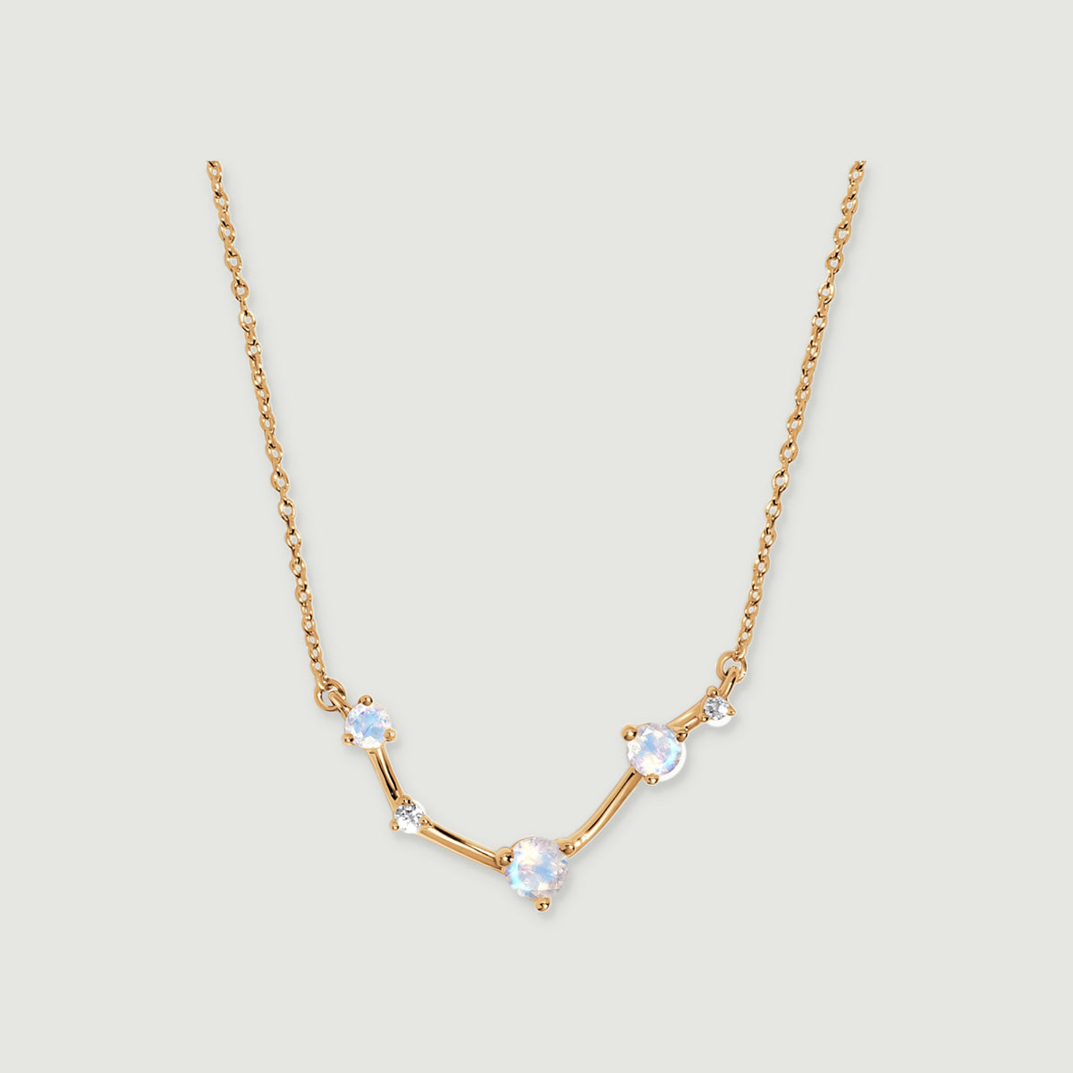 A yellow gold necklace forms a shallow curve beneath a fine chain on a pale grey background.