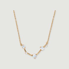 A yellow gold necklace forms a shallow curve beneath a fine chain on a pale grey background.