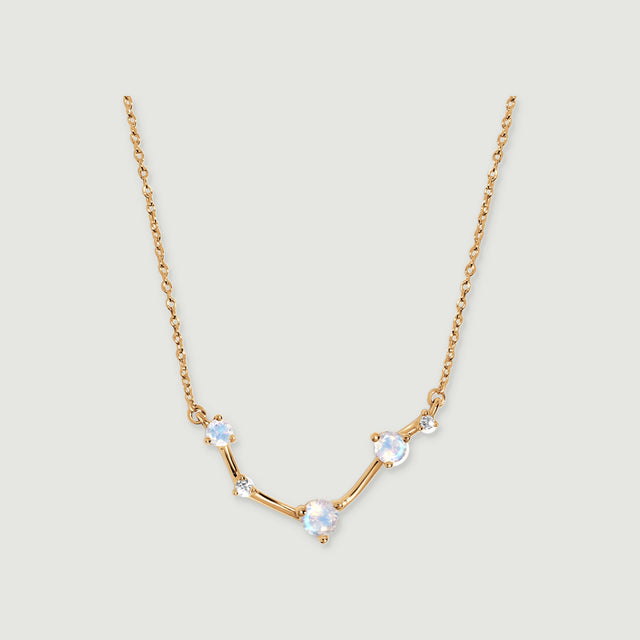 A yellow gold necklace forms a shallow curve beneath a fine chain on a pale grey background.