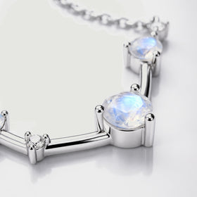 A close view shows a faceted moonstone held by silver prongs beside a small clear stone.