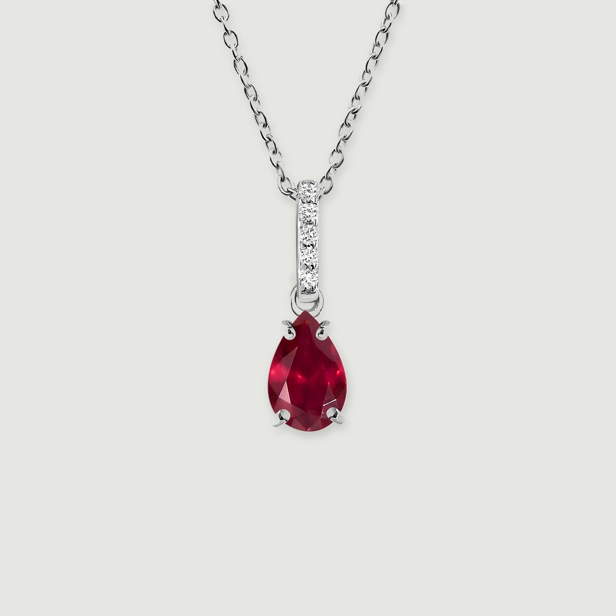 A silver chain holds a red pear-cut pendant below a narrow stone-set bail against a light gray surface.