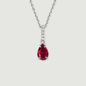 A silver chain holds a red pear-cut pendant below a narrow stone-set bail against a light gray surface.