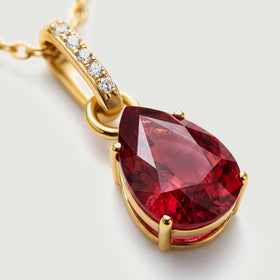 A close view shows red gemstone facets, four polished gold prongs and five clear stones along the pendant bail.