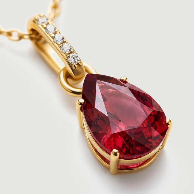A close view shows red gemstone facets, four polished gold prongs and five clear stones along the pendant bail.