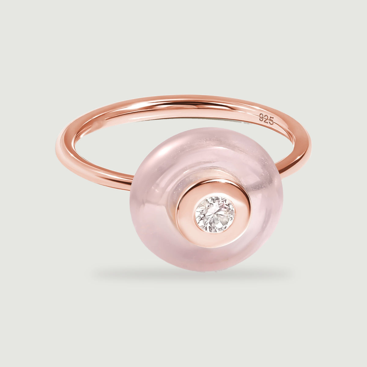 A rose gold ring displays a round pink stone and a reflective bezel around its clear center gem.