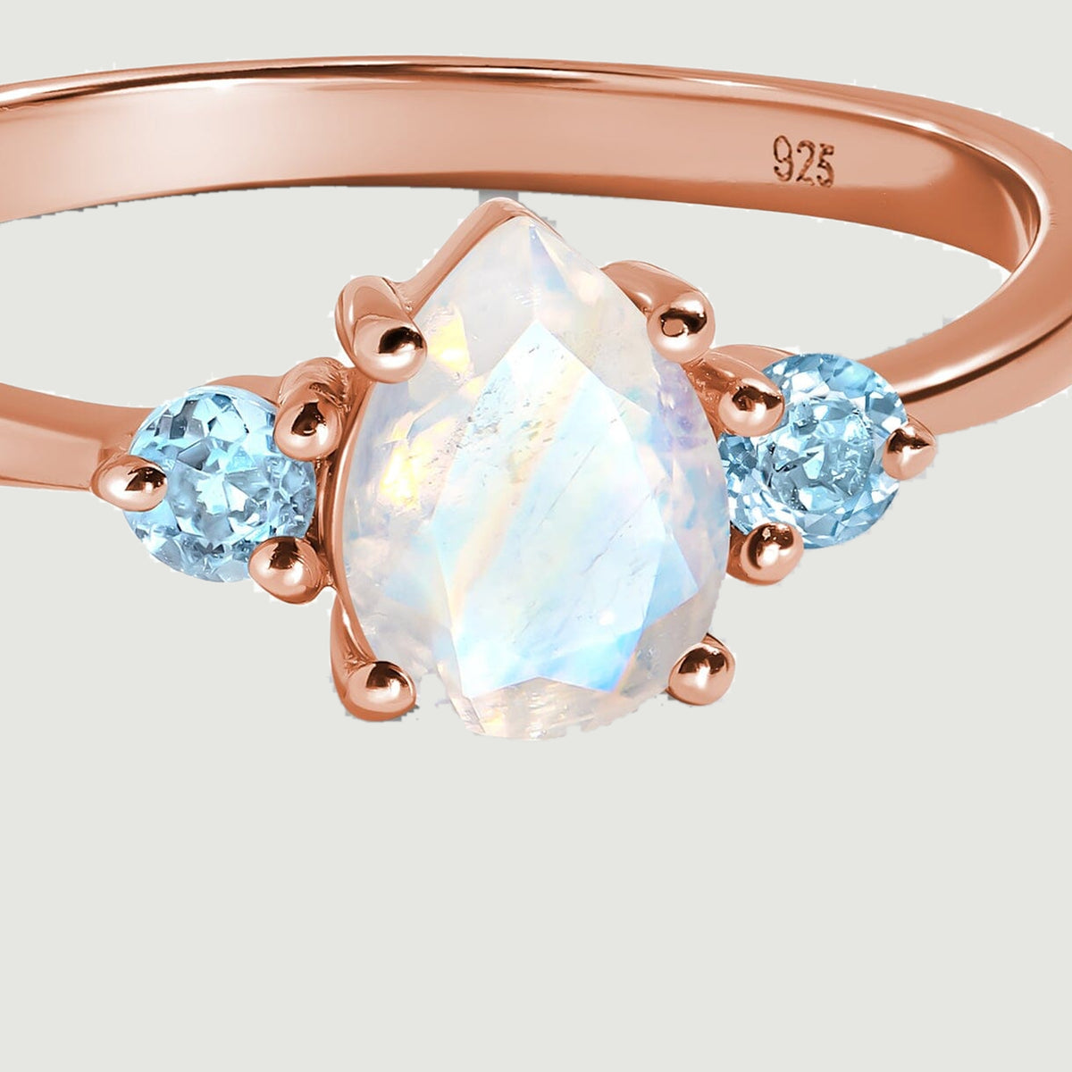A close view shows the pear-shaped moonstone facets, rose gold prongs, and two blue side stones.