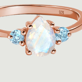 A close view shows the pear-shaped moonstone facets, rose gold prongs, and two blue side stones.