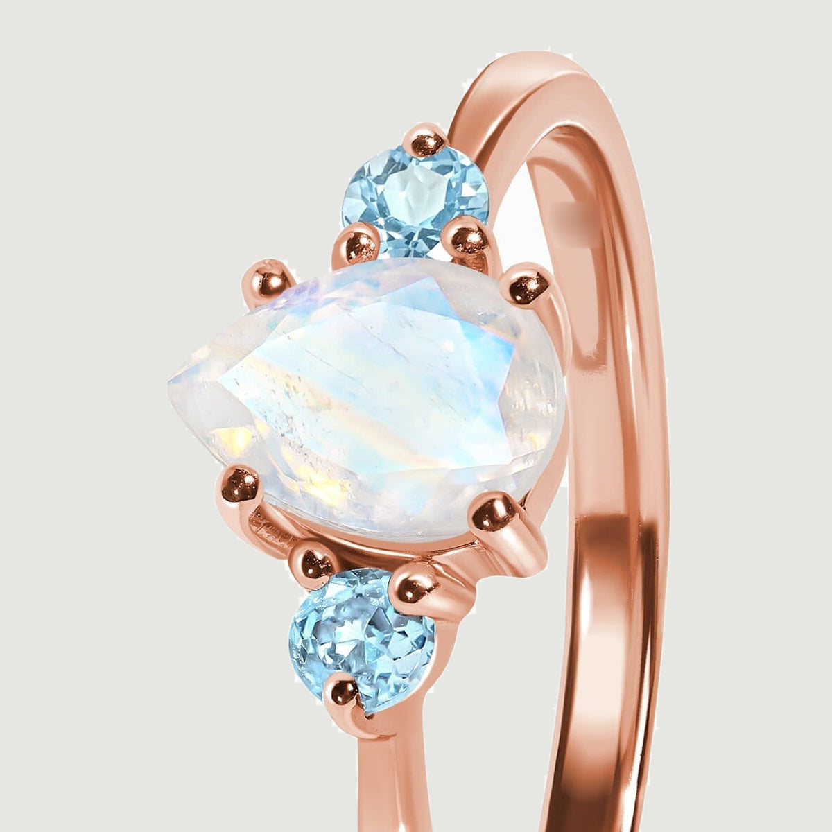 The moonstone and blue stones are shown from the side with their polished rose gold prongs.