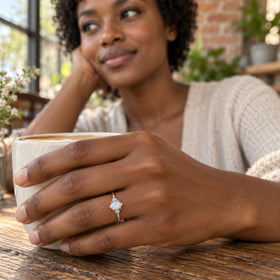 A woman with short black curls wears the rose gold moonstone ring while holding a ceramic coffee cup at a cafe table.