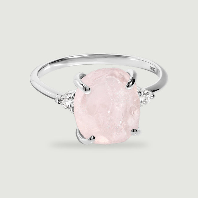 A white gold band curves behind a pale pink rough stone flanked by two small round clear stones.