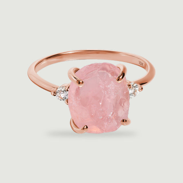 A rose gold ring surrounds a textured pink stone with four rounded prongs and clear side stones.