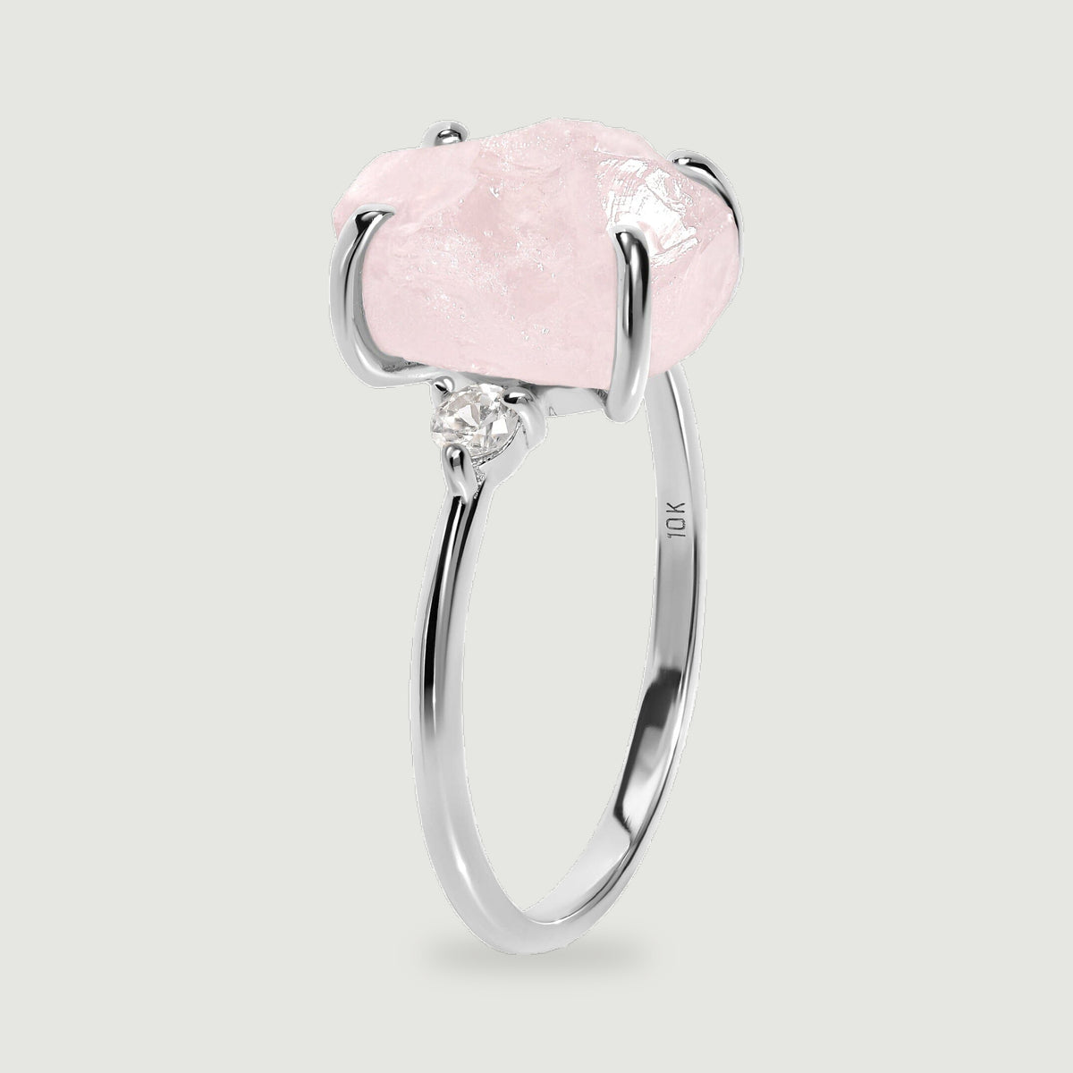 A white gold ring stands at an angle with a pale pink stone above its slender band.