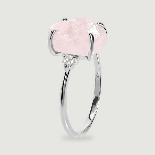 A white gold ring stands at an angle with a pale pink stone above its slender band.