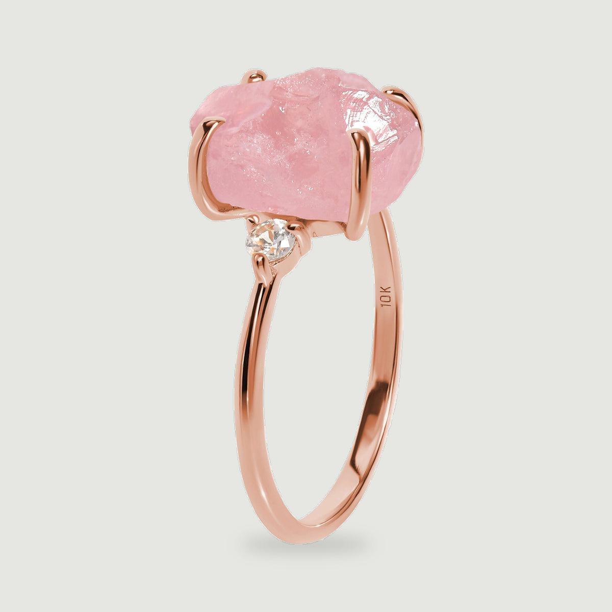 A rose gold band is shown from the side beneath a rough pink stone and a small clear stone.
